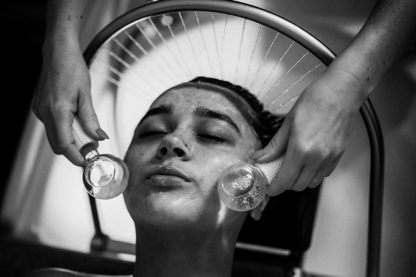 Black and white: a client under the rainfall halo with cooling globes held to her cheeks